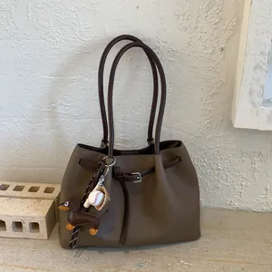 Detalle del bolso tote de cuero marrón oscuro con textura de lichi y colgantes de perro