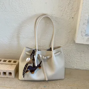 Detalle del bolso tote crema con textura de grano y colgante de perro sobre piedra