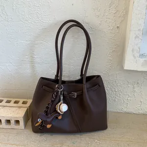 Detalle del bolso tote café oscuro con textura de lichi y colgante de cuero de perro
