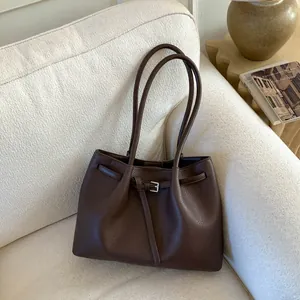 Primer plano del bolso tote de cuero marrón oscuro con hebilla plateada sobre un sofá