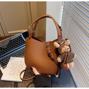 Detail of brown litchi pattern leather saddle bag with cute bear charm and strap