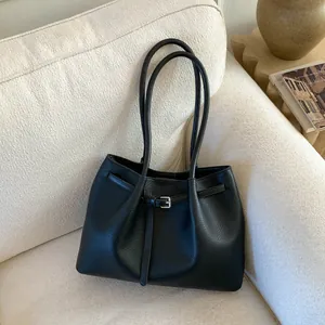 Detalle de bolso tote de cuero negro granulado con hebilla plateada en sofá