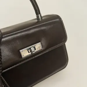 Close-up of polished dark brown leather handbag featuring a silver rectangular turn lock