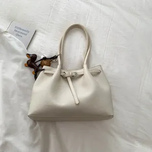 Detalle de bolso tote crema con textura litchi y colgante de teckel en tela blanca