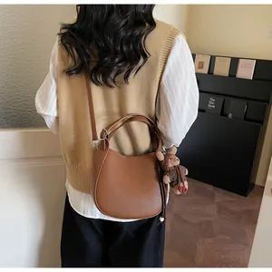 Close-up of brown pebbled leather shoulder bag with cute teddy bear plush charm detail