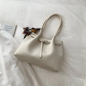 Detalle de bolso tote beige de grano lichi con colgante de perro y correa decorativa