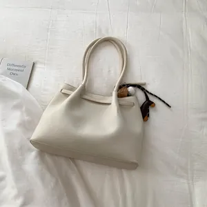 Detalle del bolso tote crema en cuero granulado con un colgante deportivo decorativo