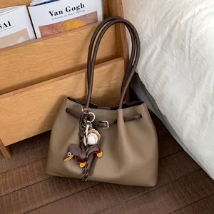 Detalle del bolso tote de cuero granulado caqui con asas marrones y colgante de perro