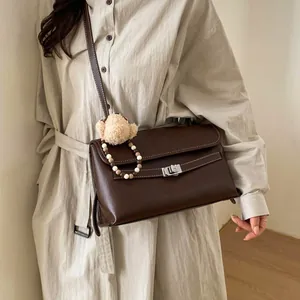 Dettaglio borsa vintage in pelle marrone con cuciture bianche e ciondolo a orso