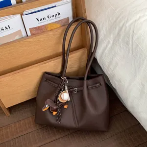 Detalle de bolso tote de cuero granulado marrón oscuro con colgantes de teckel y béisbol