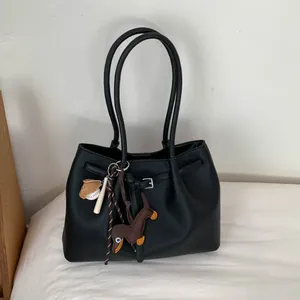 Detalle del bolso tote negro con textura de piel granulada, colgantes deportivos y hebillas de metal
