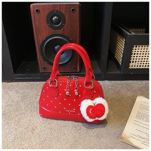Detail of red polka dot shell bag with glossy finish and plush apple charm