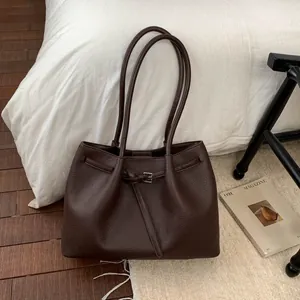 Detalle de bolso tote marrón oscuro con grano de litchi y hebilla sobre cama blanca