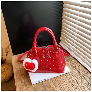 Detail of red polka dot shell bag with plush apple charm on wooden table and books