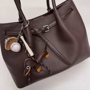 Detalle del bolso tote de cuero marrón con colgantes de béisbol y perro salchicha
