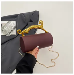 Detail of burgundy cylinder evening bag featuring a gold leopard handle and chain