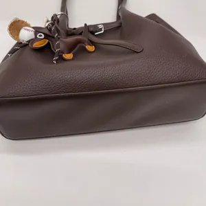 Detalle de bolso tote de cuero granulado marrón con colgante creativo de teckel
