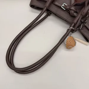 Detalle del bolso tote de cuero marrón oscuro con colgantes de béisbol decorativos