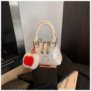 Close-up of cream polka dot handbag with a red apple plush charm and silver hardware