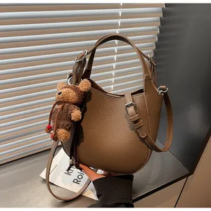 Close-up of brown litchi grain leather texture on handbag with a cute teddy bear charm