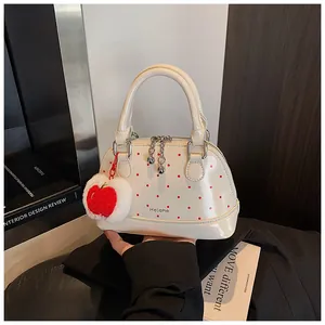 Detailed view of a white shell handbag with red polka dots and a cute apple charm