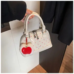 Close-up of cream shell handbag with red polka dots and apple plush charm detail