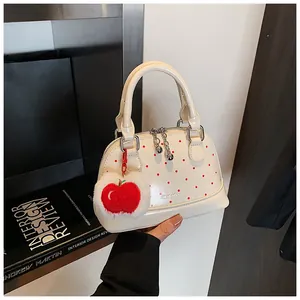 Detail of cream shell handbag with red polka dots and apple plush charm