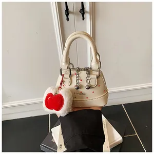 Close-up of white shell bag with red polka dots, logo text, and plush apple charm accessory