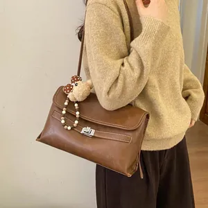 Dettaglio della borsa tote marrone vintage con cuciture bianche e ciondolo a orso