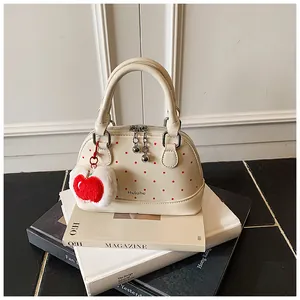 Detail of cream shell handbag with red polka dots and cute apple plush charm on books