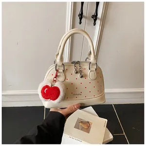 Detail of off-white polka dot shell handbag with red apple plush charm and dual handles