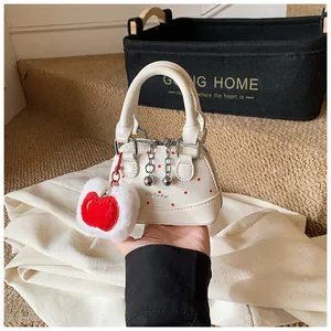 Close-up of a mini off-white shell handbag with red polka dots and a red apple plush charm