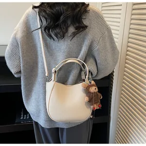 Detail view of cream bucket bag with lychee grain texture and cute bear charm pendant