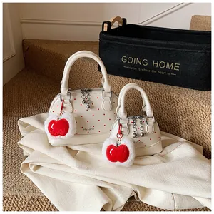 Detail view of white shell-shaped handbags with red polka dots and apple plush charms