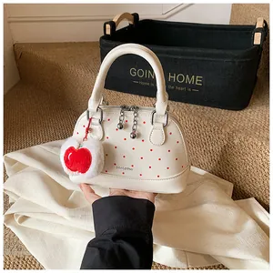 Close-up of white leather shell bag with red dots and a plush apple pendant detail
