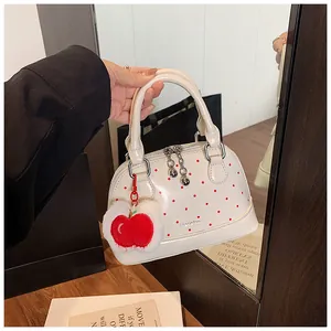 Detail of white shell handbag with red polka dots and decorative apple plush charm