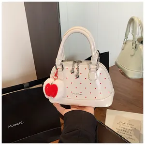 Detail of white polka dot shell bag featuring a red apple plush charm and dual zippers