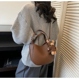 Detail of dark brown leather crescent bag featuring a cute plush bear charm accessory