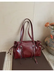 Detail of dark red oil wax leather tote bag with drawstring closure and silver zippers