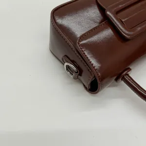 Detail of glossy brown leather handbag with silver D-ring hardware and top handle
