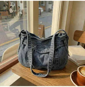 Détails du sac bandoulière en denim lavé avec logo embossé sur une table de café en bois