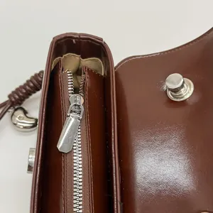 Macro detail of glossy brown leather bag showing silver zipper and bean-shaped pendant