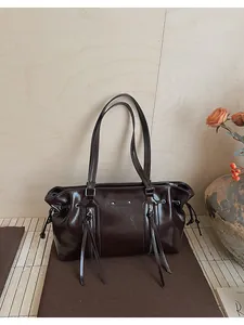 Detail of dark brown glossy patent leather tote bag with vertical zipper and drawstring