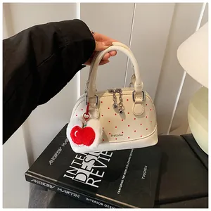 Close-up of white polka dot shell bag with cherry charm and brand logo detail