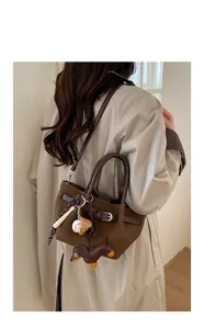 Detail einer dunkelbraunen Vintage-Eimertasche mit Anhängern auf einem Trenchcoat