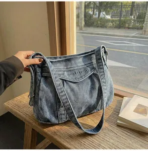 Détail du sac cabas en jean bleu avec broderie posé sur un banc en bois
