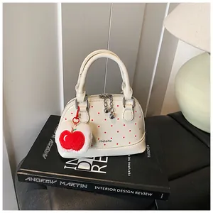 Detailed view of cream polka dot shell bag with red apple plush charm on a design book