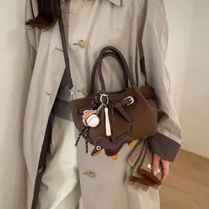 Detail der kaffeebraunen Tasche mit Hundeanhänger und Baseball-Deko am beigen Trenchcoat