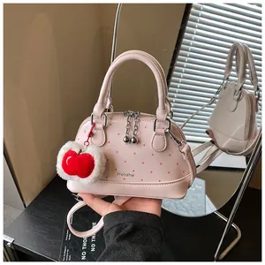 Detail of pink polka dot shell bag with plush apple charm and metallic zipper ball