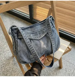 Détail du sac bandoulière en denim bleu avec broderie SUBELETING blanche sur une chaise